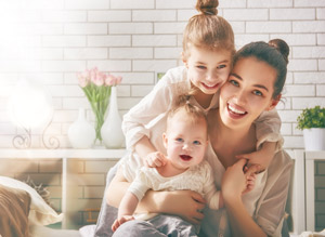 Picture of a young mother with her two daughters (one toddler and one baby) They are hugged up together and smiling,